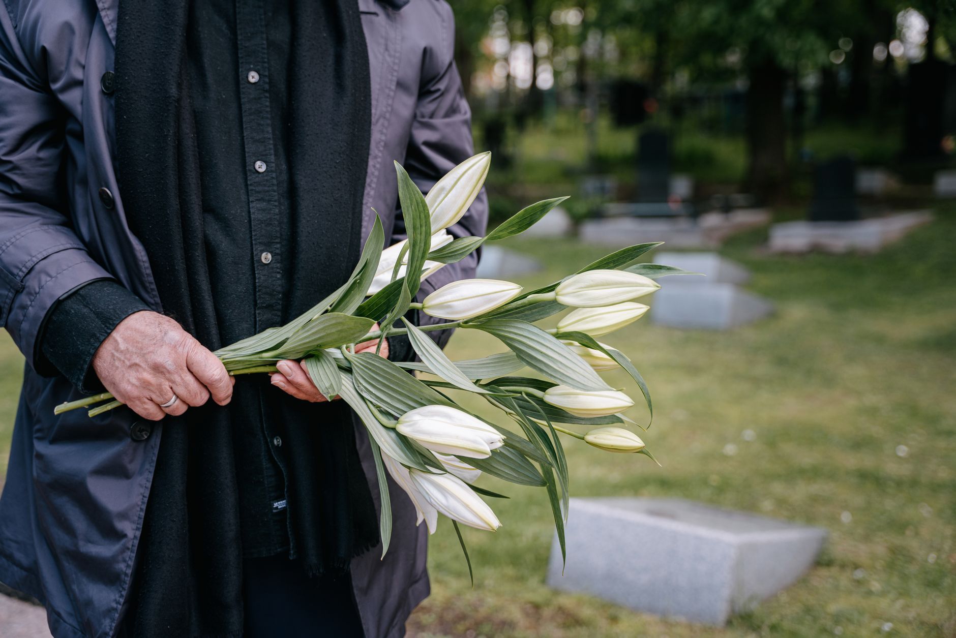 A person holding a bouquet of white lilies at a graveside ceremony